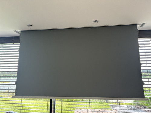SCREENLINE 108″ motorizuotas projekcinis ekranas, įmontuotas lubose ir nuleistas priešais langus.
